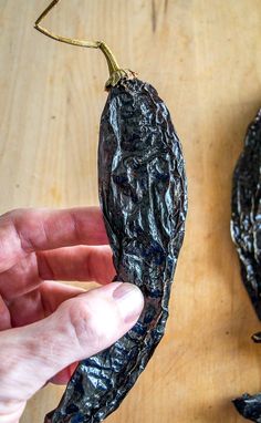 a person holding an open black pepper on a wooden table next to it's peel