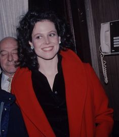 a woman in a red coat standing next to an older man