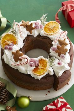 a chocolate cake with orange slices and white frosting on a green table next to christmas decorations