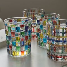 several colorful glass cups sitting on top of a table next to an open book and pen