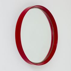 a round mirror mounted to the side of a white wall next to a red shelf