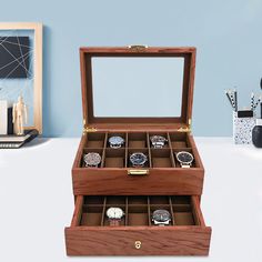 an open wooden watch box on a white table next to a blue wall and vase