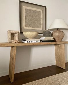 a wooden table topped with books next to a lamp and painting on the wall behind it