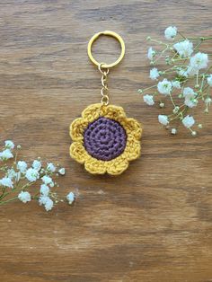 a crocheted flower keychain sitting on top of a wooden table next to flowers