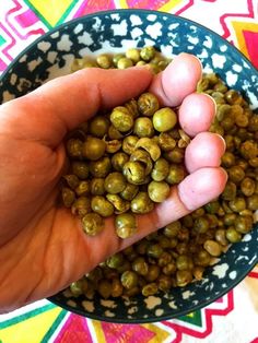 a hand is holding some green peas in a bowl on a colorful table cloth,