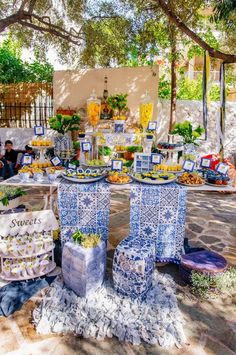 an outdoor table with blue and white plates on it, surrounded by flowers and other decorations