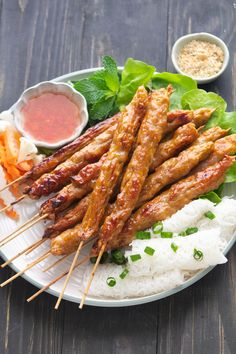 several skewers of meat on a plate with rice and vegetables next to dipping sauces