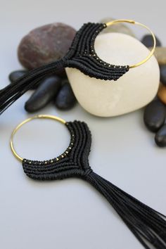 a pair of black tasseled earrings sitting on top of a white table next to rocks