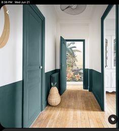 an empty hallway with green doors and wooden floors in front of a mirror on the wall