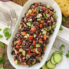 a white platter filled with black beans and cucumbers next to sliced bread