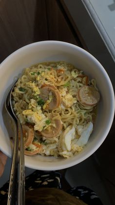 a white bowl filled with noodles and meat on top of a table next to a fork