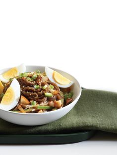 a white bowl filled with noodles, hard boiled eggs and sliced green onions on top