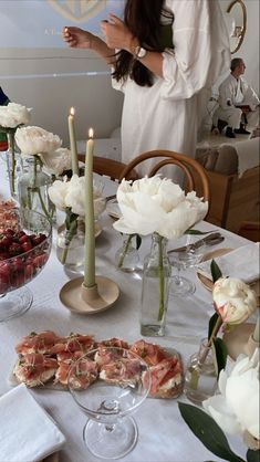 a woman standing in front of a table filled with food and flowers on top of it