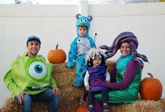 three adults and two children dressed up as monsters sitting on hay bales with pumpkins