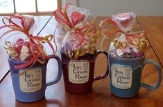 three coffee mugs filled with candy and wrapped in ribbon, sitting on a table