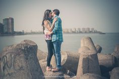 a man and woman kissing on the rocks by the water