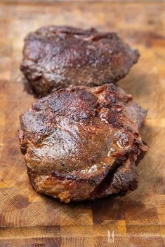 two pieces of meat sitting on top of a wooden cutting board