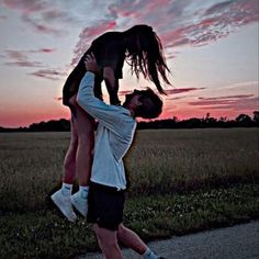 two people are playing with each other in the grass at sunset or dawn, one person is lifting another man over his head