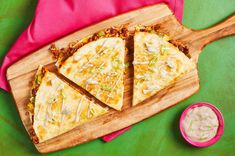 three slices of pizza on a wooden cutting board next to a small bowl of dip