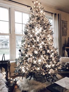 a decorated christmas tree in front of a window with white lights and ornaments on it