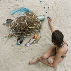 a woman sitting in the sand next to a turtle covered in seaweed and other items