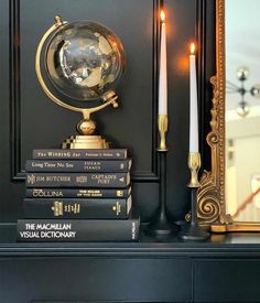 a black mantle with books and a gold globe on top, next to a candle