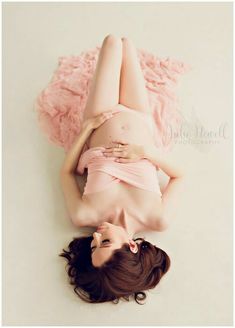 a pregnant woman laying on top of a pink blanket