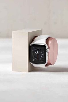 an apple watch sitting in a box on top of a white surface with a pink ring around it