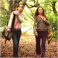 two girls walking down a leaf covered path in the woods, one carrying a backpack and the other carrying a purse