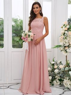 a woman in a long pink dress standing next to some white flowers and greenery