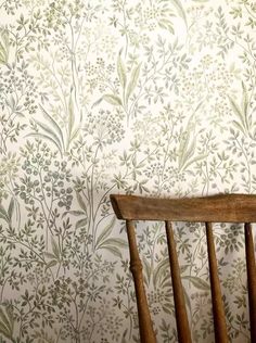 a wooden chair sitting in front of a wallpapered with green and white flowers