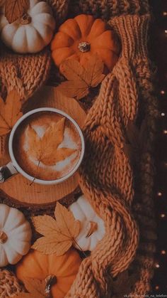 a cup of coffee on top of a wooden board surrounded by pumpkins and leaves