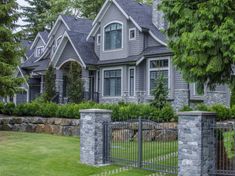 a gray house with stone walls and gate in the front yard, surrounded by lush green trees