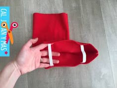 a hand holding a red santa hat on top of a wooden floor