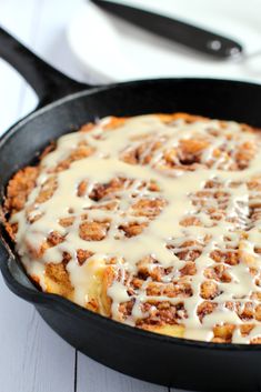 a skillet filled with cinnamon rolls covered in icing on top of a white table