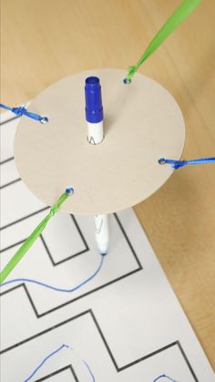 a table with some blue and green string attached to the top, on which there is a white piece of paper that has been cut into smaller pieces