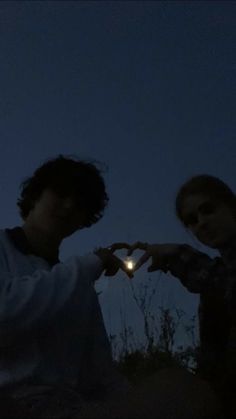 two young men are standing outside at night with their hands in the shape of a heart