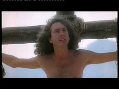 a shirtless man holding a wooden pole with his arms spread out to the side