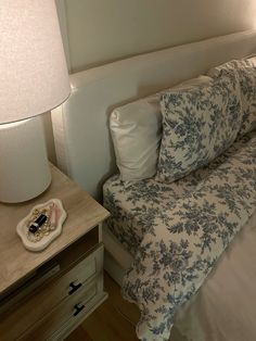 a bed with blue and white floral bedspread next to a lamp on a night stand