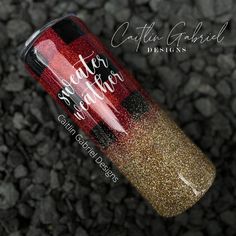 a red and gold glitter nail polish with black tips on it, next to some rocks