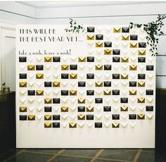 a white wall with gold and black envelopes on it, next to a potted plant