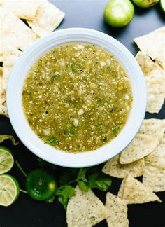 a white bowl filled with green salsa surrounded by tortilla chips and limes