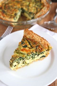 a slice of quiche on a plate next to a fork and glass pie dish