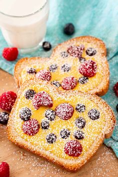 two pieces of bread with berries and powdered sugar on them next to a glass of milk