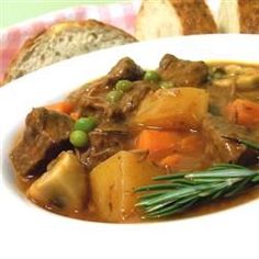 a white bowl filled with beef stew and vegetables on top of a table next to bread