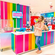 a woman standing in front of a candy store counter with rainbow stripes on the wall