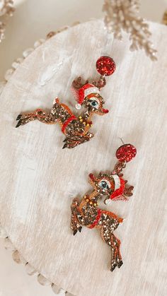 two red and gold reindeer brooches sitting on top of a white cloth covered table