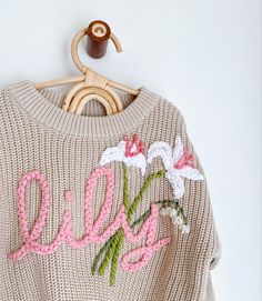 a sweater with flowers is hanging on a wooden hanger and has the word love written in pink