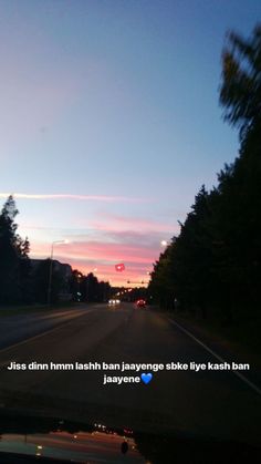 the sun is setting on an empty street with trees in the foreground and a red traffic light above it