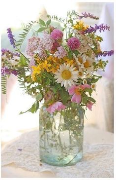 a glass vase filled with lots of flowers on top of a white table covered in lace